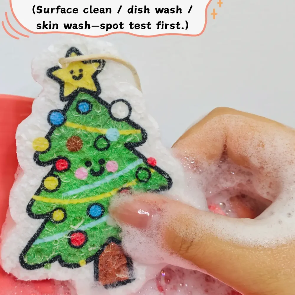 Christmas tree cellulose sponge being used to wash a dish on a red plate with foam and water.