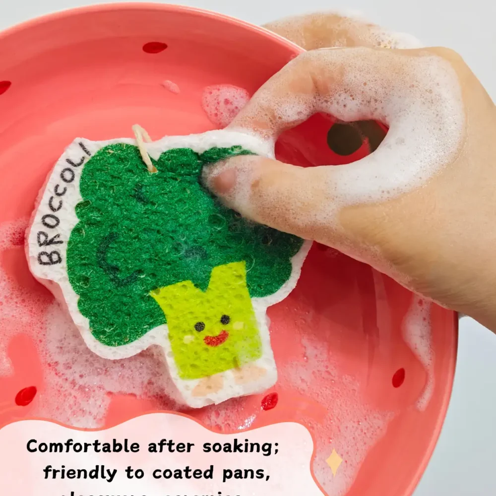 Broccoli-shaped cellulose sponge being used to wash a dish on a red plate with foam and water.