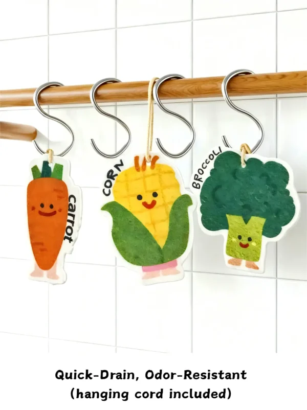 Carrot, corn, and broccoli cellulose sponges hanging from white hooks by their cords to dry.